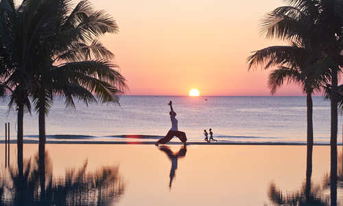 Sunrise over Danang beach with woman doing Yoga with her reflection reflecting in the infinity pool